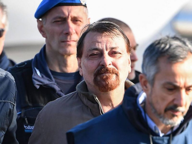 Italian former communist militant Cesare Battisti (C), wanted in Rome for four murders attributed to a far-left group in the 1970s, is escorted by Italian Police officers after stepping off a plane coming from Bolivia and chartered by Italian authorities, after landing at Ciampino airport in Rome on January 14, 2019. Former communist militant Cesare Battisti landed in Rome on January 14 after an international police squad tracked the Italian down and arrested him in Bolivia, ending almost four decades on the run.  / AFP / Alberto PIZZOLI